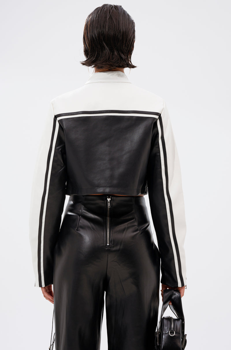 A person faces away, wearing the WEST LOOP RACER MOTO jacket with vertical sleeve stripes and high-waisted shiny faux leather black pants, holding a small black handbag in their left hand.