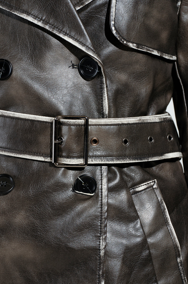 Close-up of the ACID RAP FAUX LEATHER TRENCH, featuring dark faux leather with double-breasted button closures, white piping along the seams, and a wide belt with a silver buckle. The material has a glossy finish, emphasizing the texture and craftsmanship.