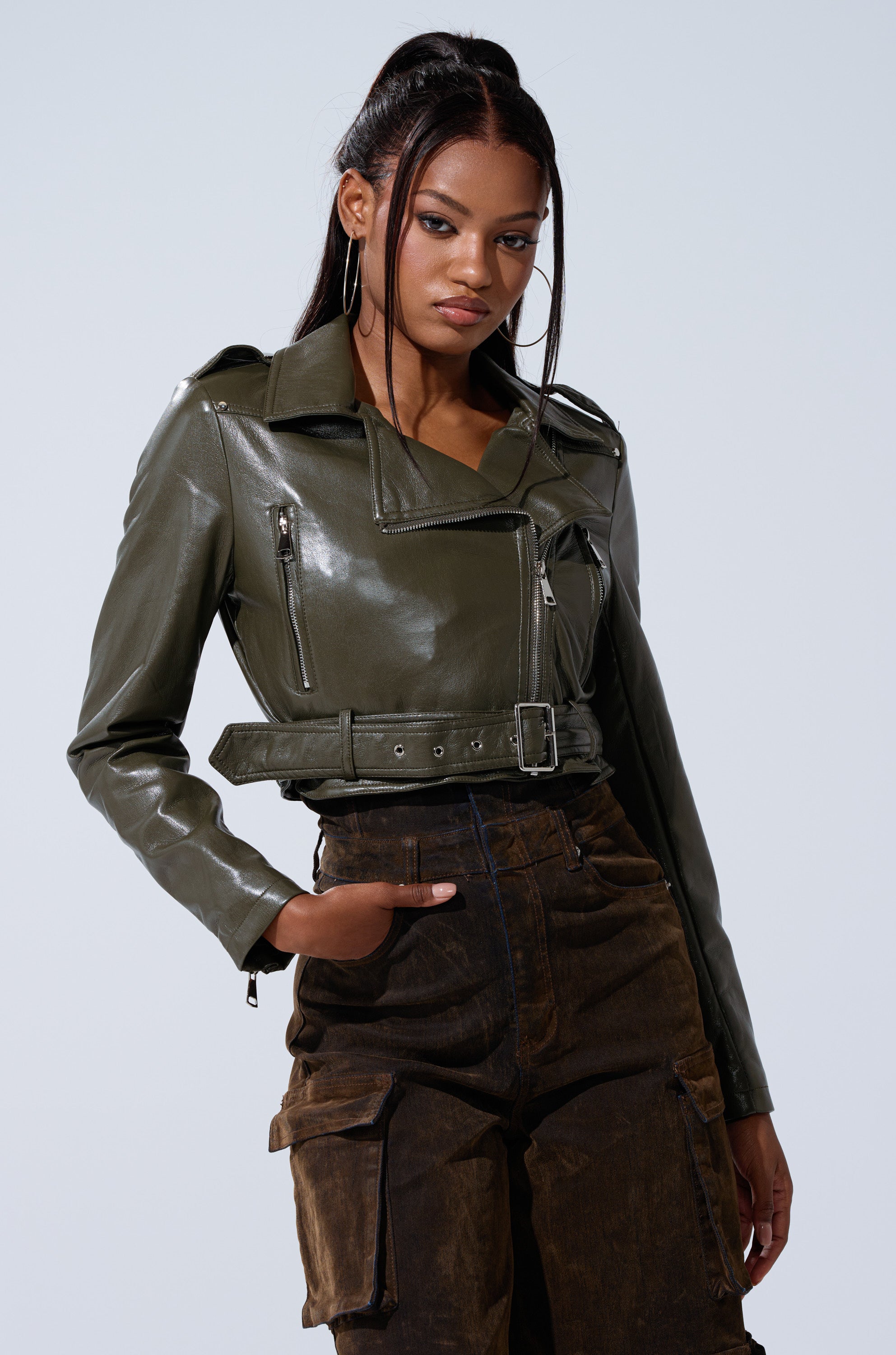 A woman with long dark hair in a high ponytail poses confidently against a light background, wearing the BUTTER LUXE EVERYDAY MOTO jacket and high-waisted brown cargo pants, with one hand in her pocket.