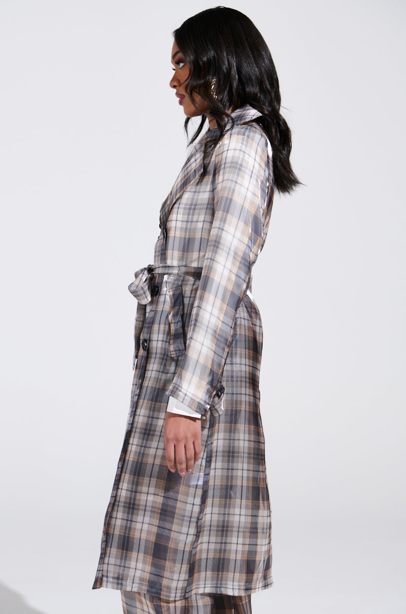 A person with long dark hair wears the "PLAID ABOUT YOU SHEER TRENCH," a plaid coat in shades of gray, white, and brown with a waist belt. They stand in profile against a plain white background.