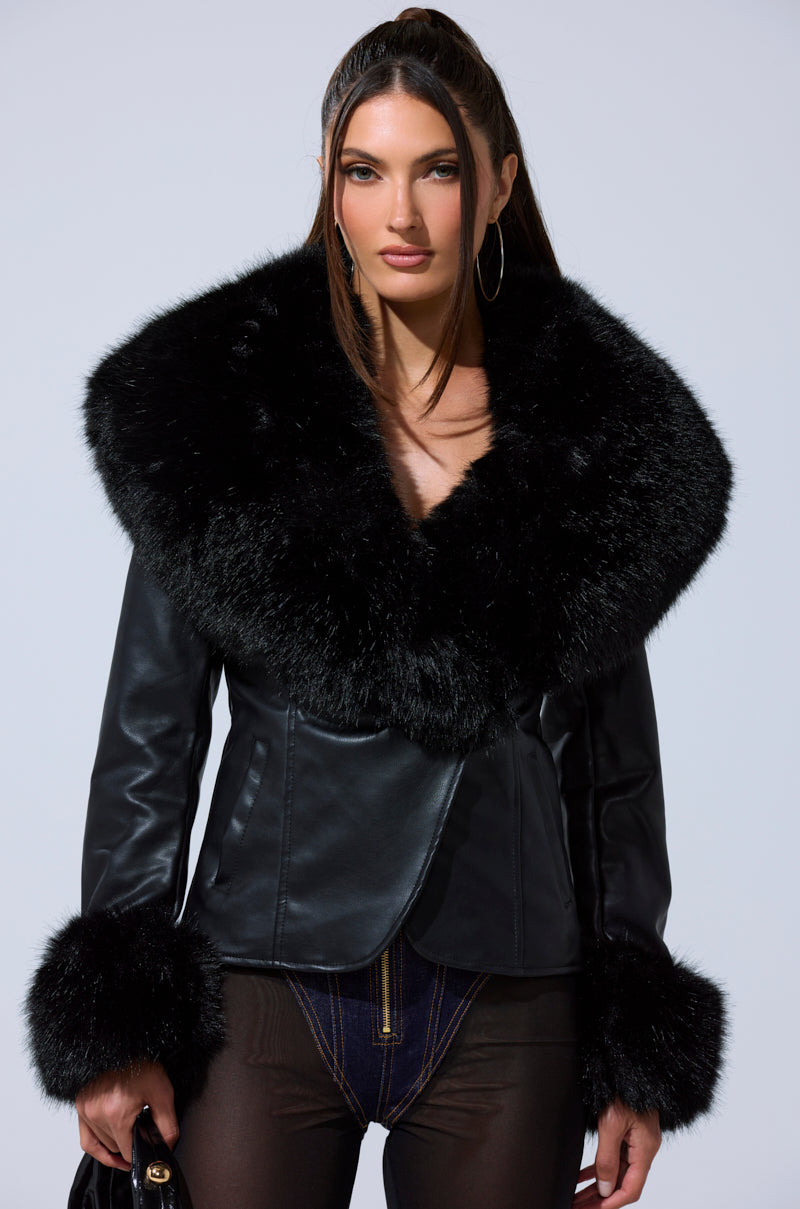 A woman with sleek long brown hair wears the CELESTE FUR TRIM BLAZER featuring a chic design with large, fluffy black faux fur collar and cuffs, posing against a light background and looking at the camera.