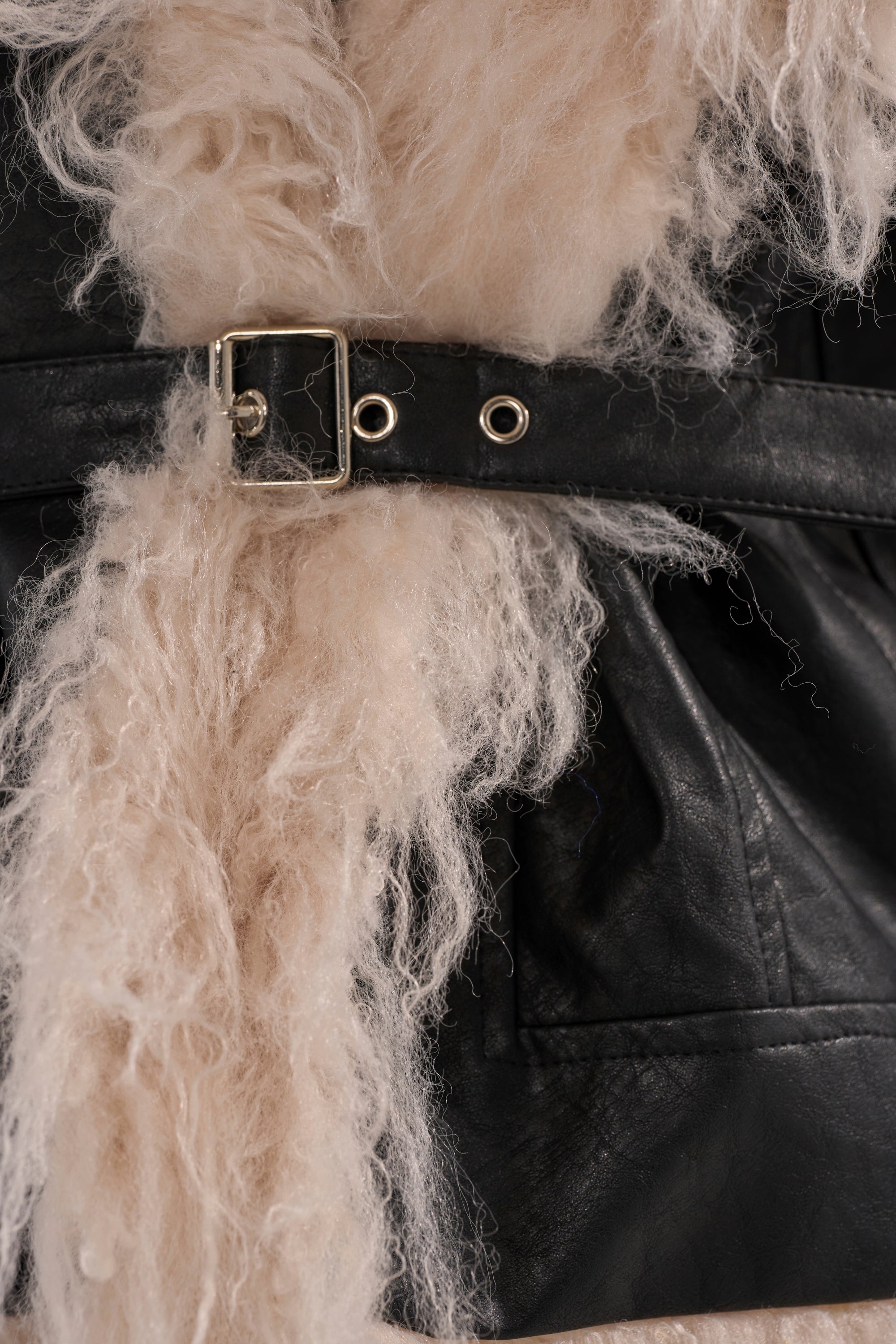 Close-up of the ROSIE FUR TRIM MOTO, a black leather moto jacket featuring a silver buckle and cream curly faux fur trim.