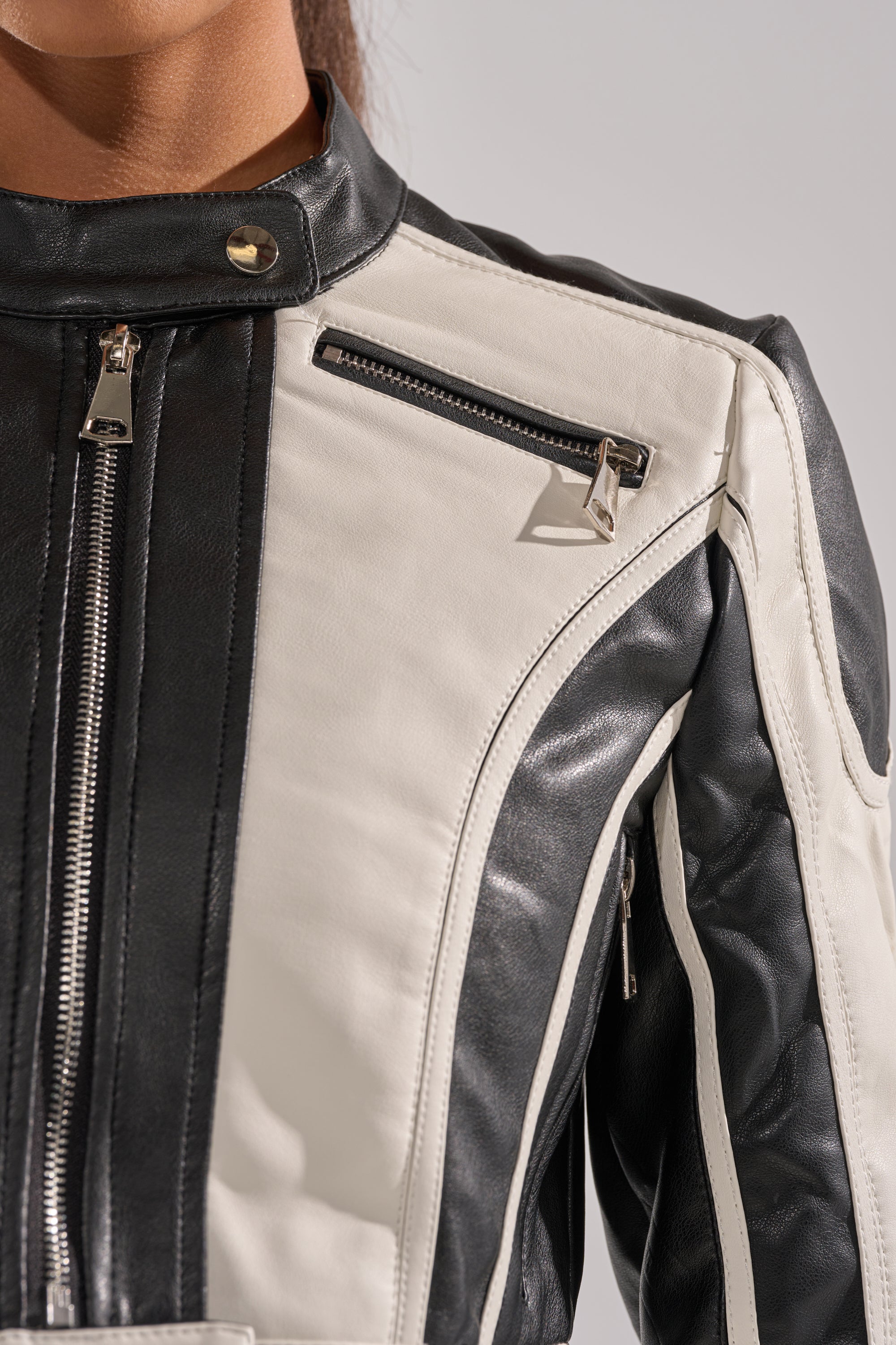 Close-up of a person wearing the BETTER LUCK CROPPED MOTO IN BLACK WHITE, featuring black and white faux leather, zippers, snap buttons, and contrasting panel details. The person's face is partially visible. 8