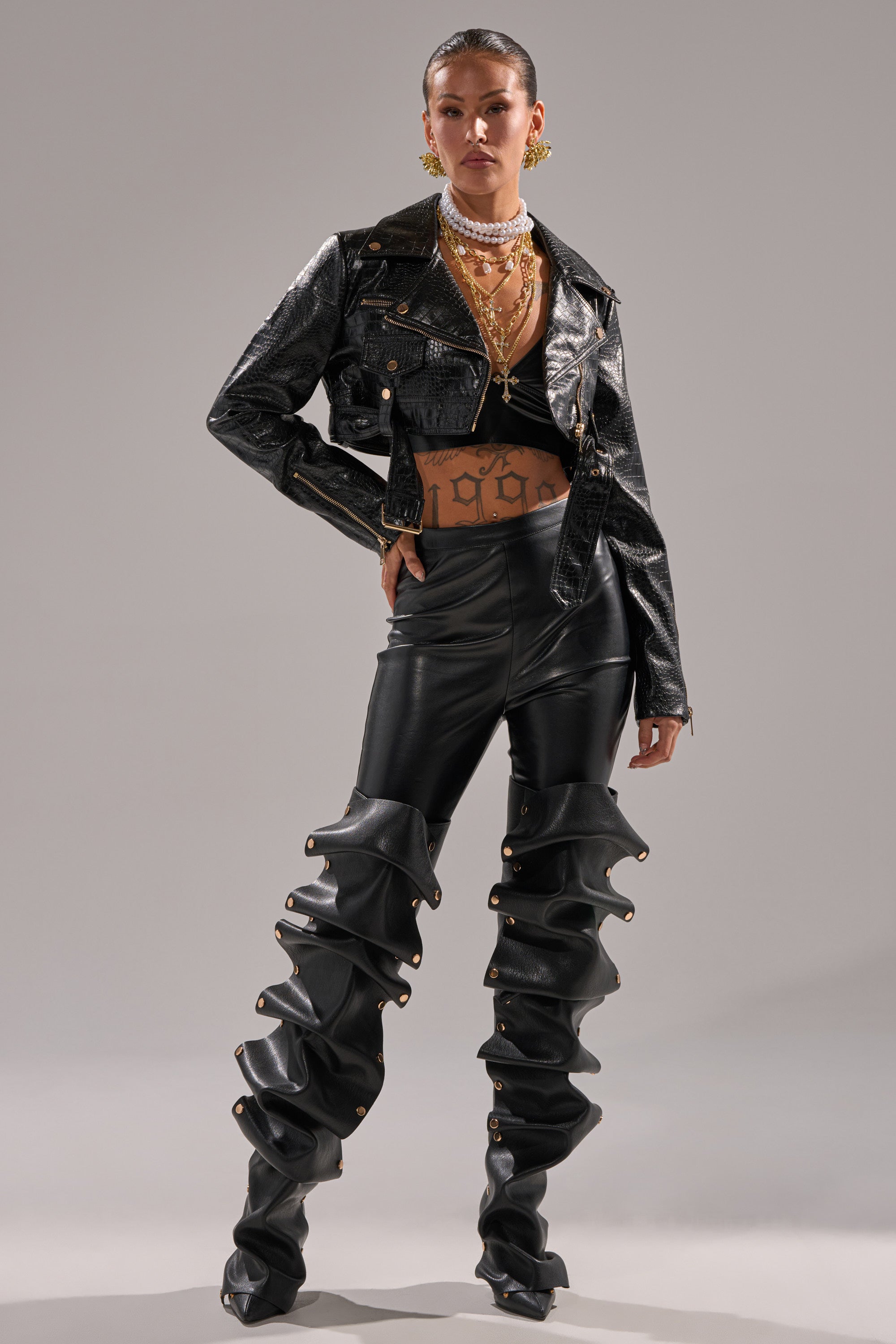 A person poses confidently in the EVERYDAY MOTO IN BLACK CROC jacket, paired with high-waisted pants with dramatic ruffled legs, layered gold jewelry, and a sleek ponytail against a plain background. 7
