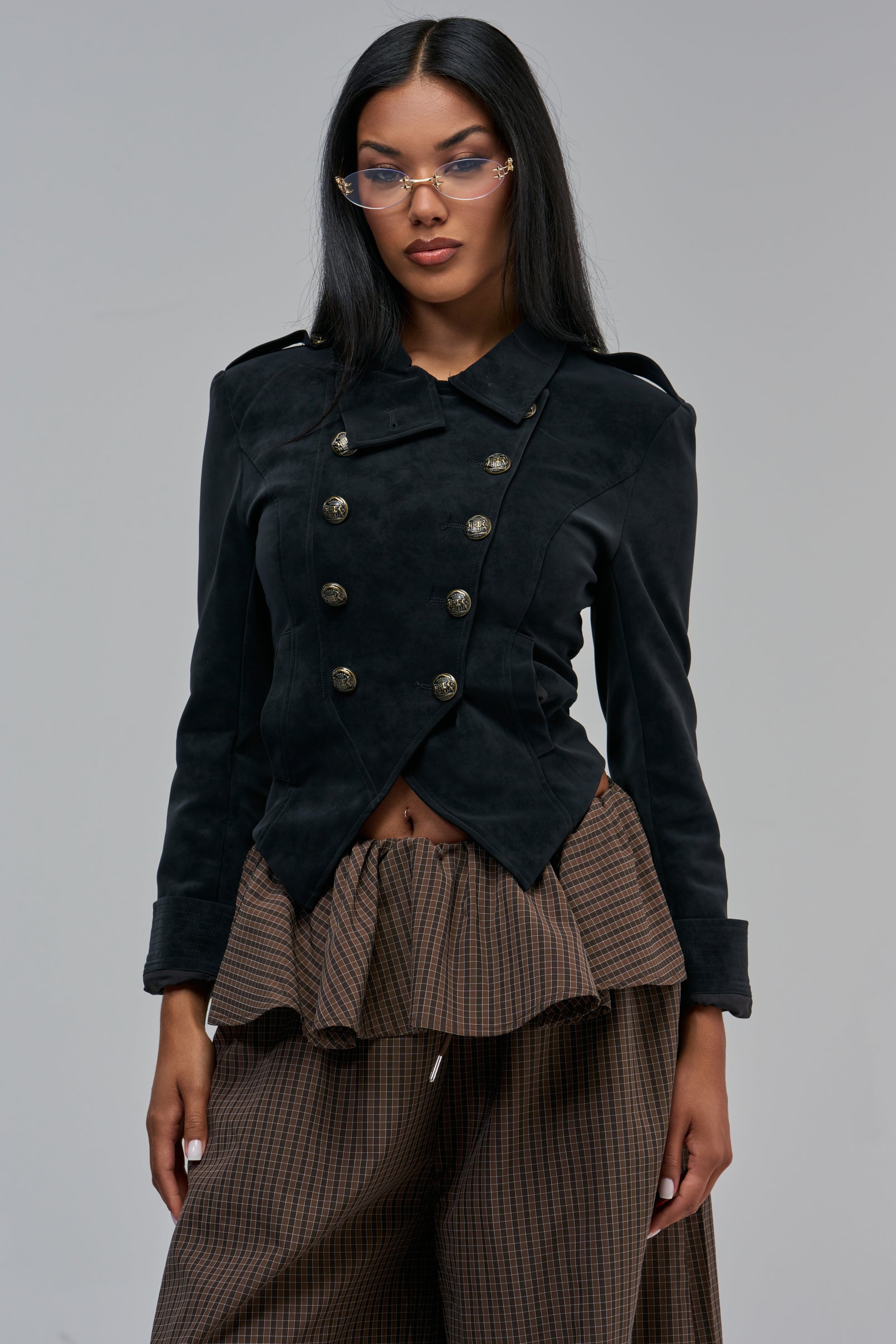 A person wears an AIMEE MILITARY MOTO black faux leather jacket with double-breasted gold buttons and a collared neckline over a brown plaid, high-waisted skirt in this streetwear styling.
