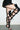 A person wearing a short black skirt and AZALEA WANG KRISTINE BLACK STRAPPY UPPER GLADIATOR SANDALS with stiletto heels, one leg raised against a plain white wall.