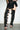 A person wears a short, sheer black skirt and the AZALEA WANG KRISTINE BLACK STRAPPY UPPER GLADIATOR SANDAL with lace-up thigh-high design and open toes, standing against a plain white wall.