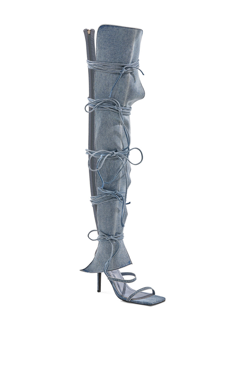 The AZALEA WANG KRISTINE DENIM STILETTO GLADIATOR SANDAL is a single thigh-high denim boot featuring an open square toe and multiple long laces wrapped around the shaft, shown against a white background.