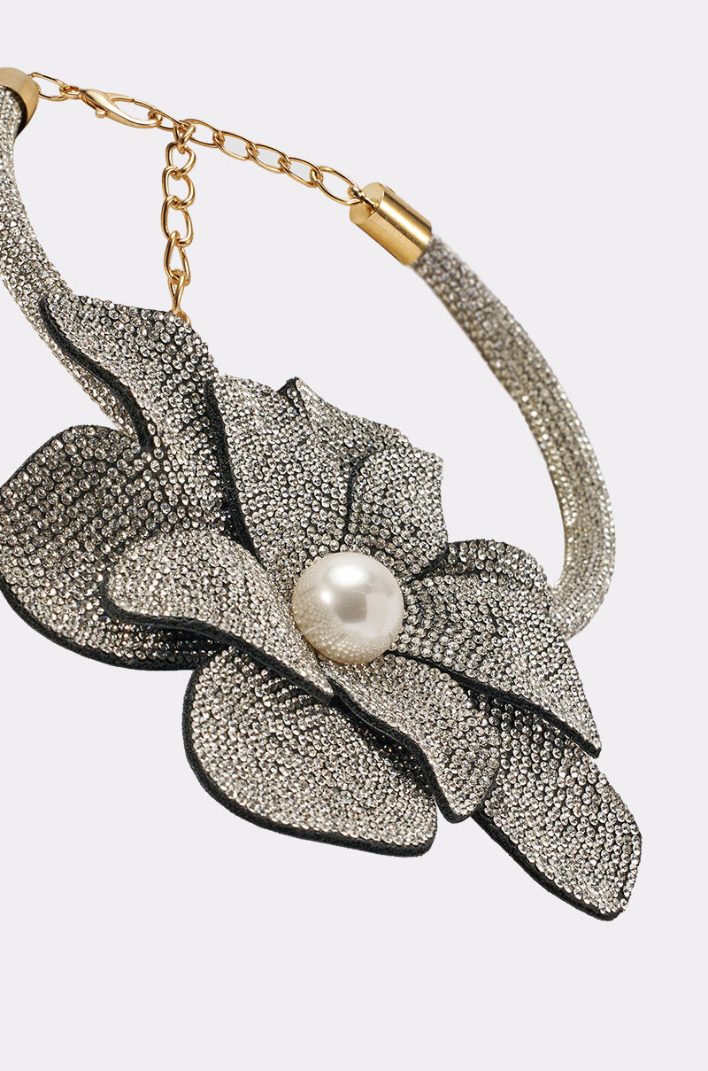 A close-up of the HOLIDAY READY NECKLACE, featuring a sparkling silver floral pendant with a large pearl center, gold chain and clasp details, and delicate jeweled accents displayed on a light background. 3
