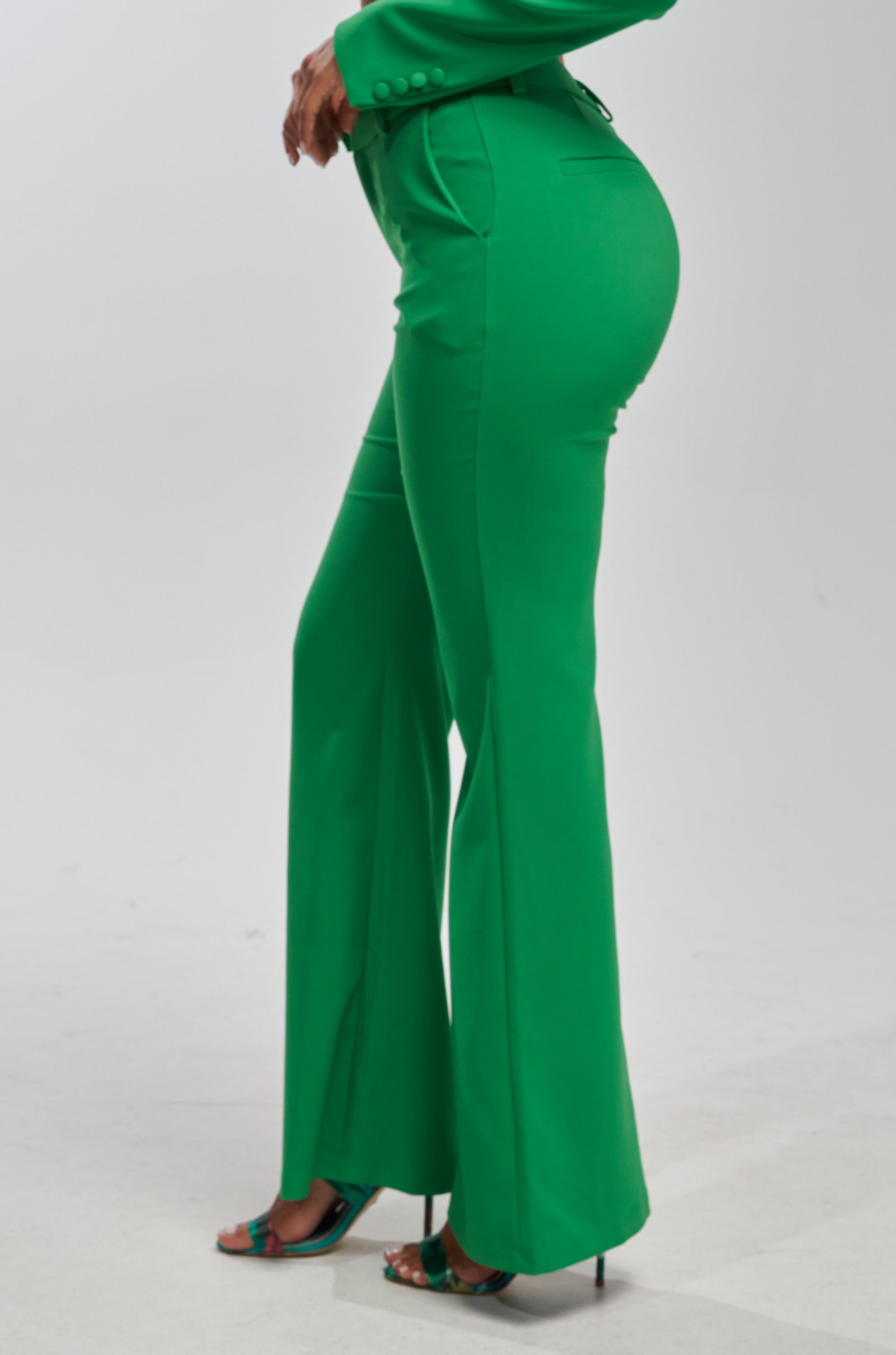 Wearing the JUST YOUR LUCK FLARE TROUSER IN GREEN, a person stands against a plain white background with only their lower half visible, paired with heeled sandals.