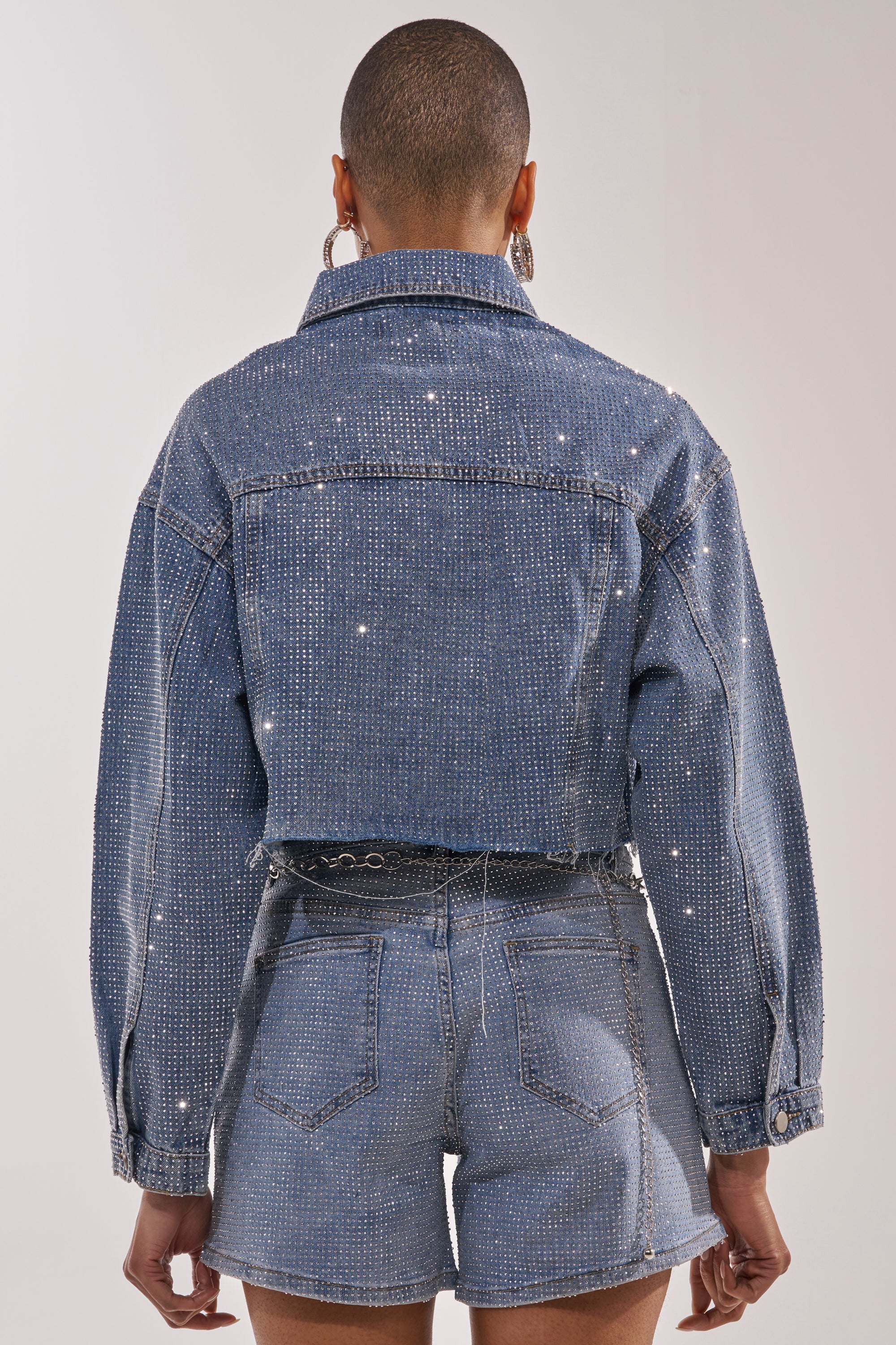 A person with short hair, seen from behind, wears the KYLIE EMBELLISHED DENIM JACKET paired with matching high-waisted rhinestone shorts against a plain light background. 7