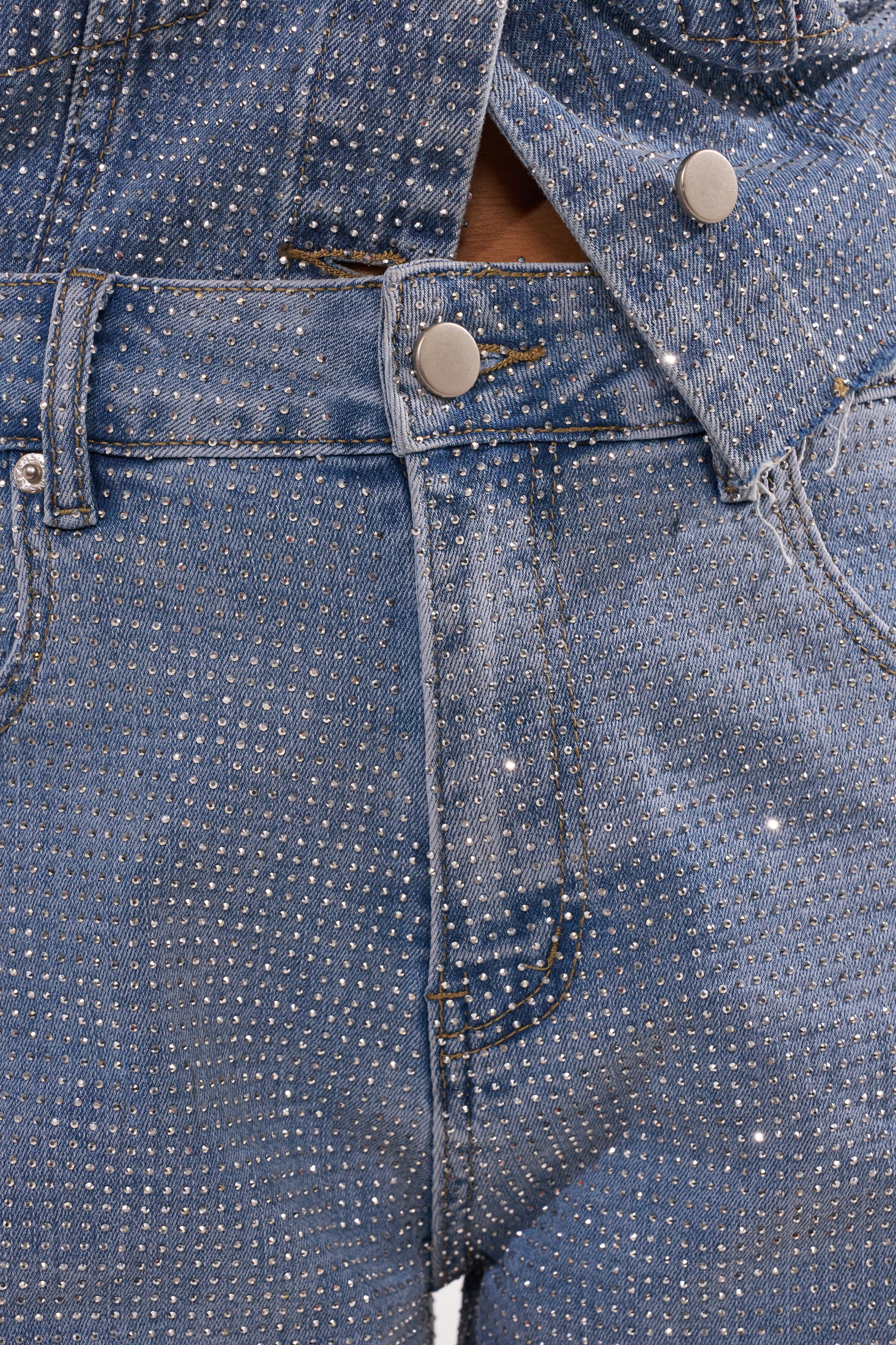 Close-up of blue denim jeans and a matching jacket adorned with silver rhinestones and metallic buttons—perfectly complementing your KYLIE EMBELLISHED DENIM SHORT. 8