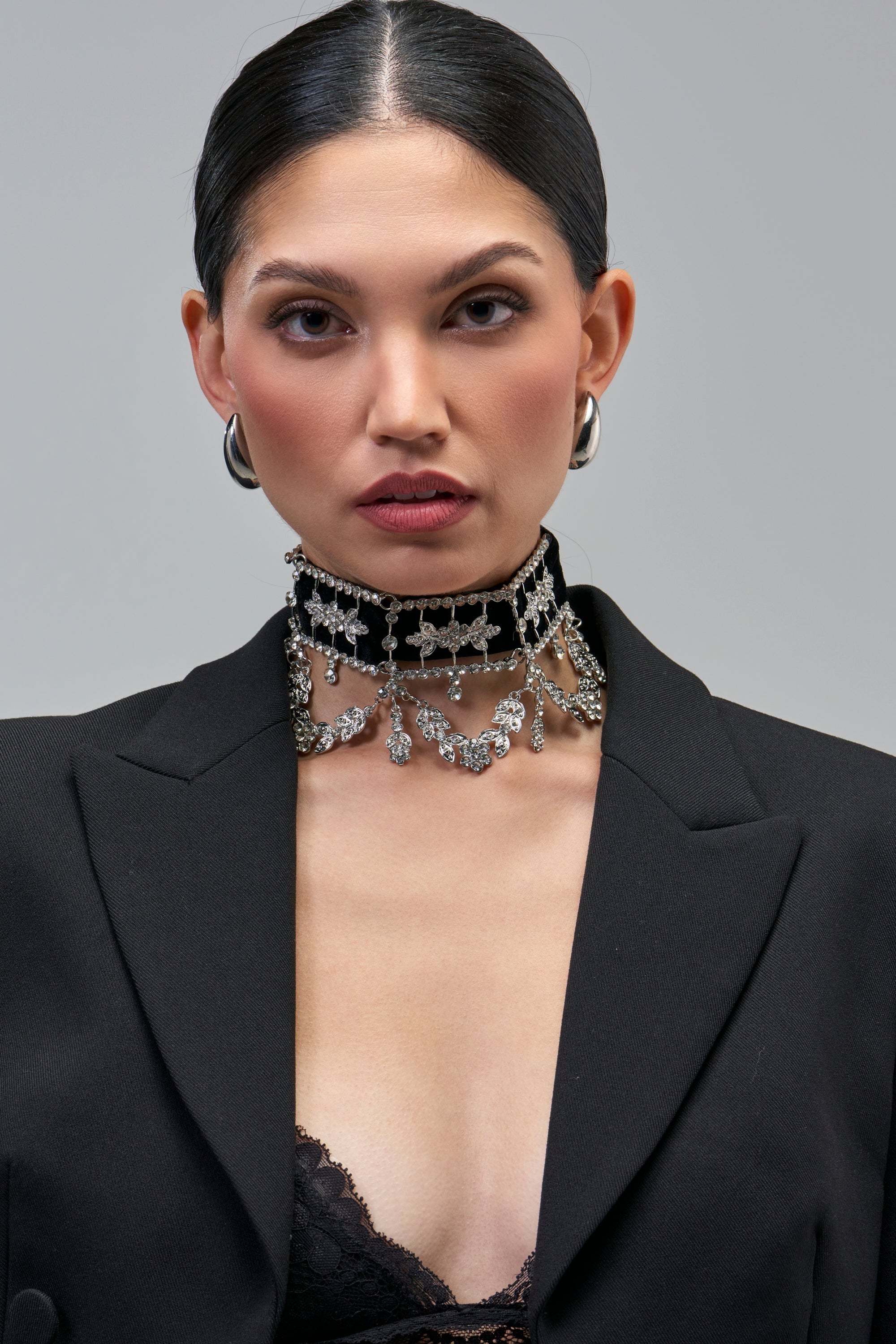 A person wears a WHERES THE PARTY CHOKER NECKLACE, a vintage-inspired black velvet choker embellished with silver-tone floral-shaped rhinestones and hanging crystal pendants.