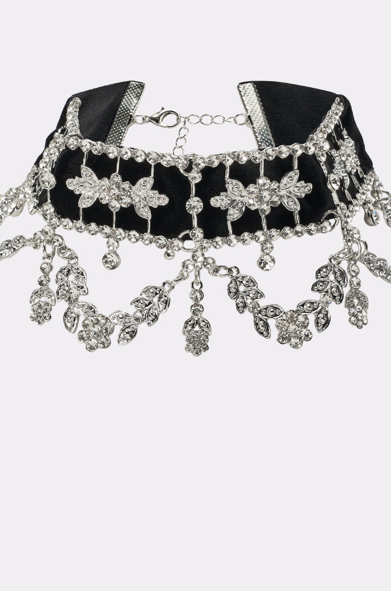 The WHERES THE PARTY CHOKER NECKLACE is a black velvet choker with silver floral and leaf-shaped crystal accents, vintage-inspired dangling charms, and an adjustable chain clasp. 2