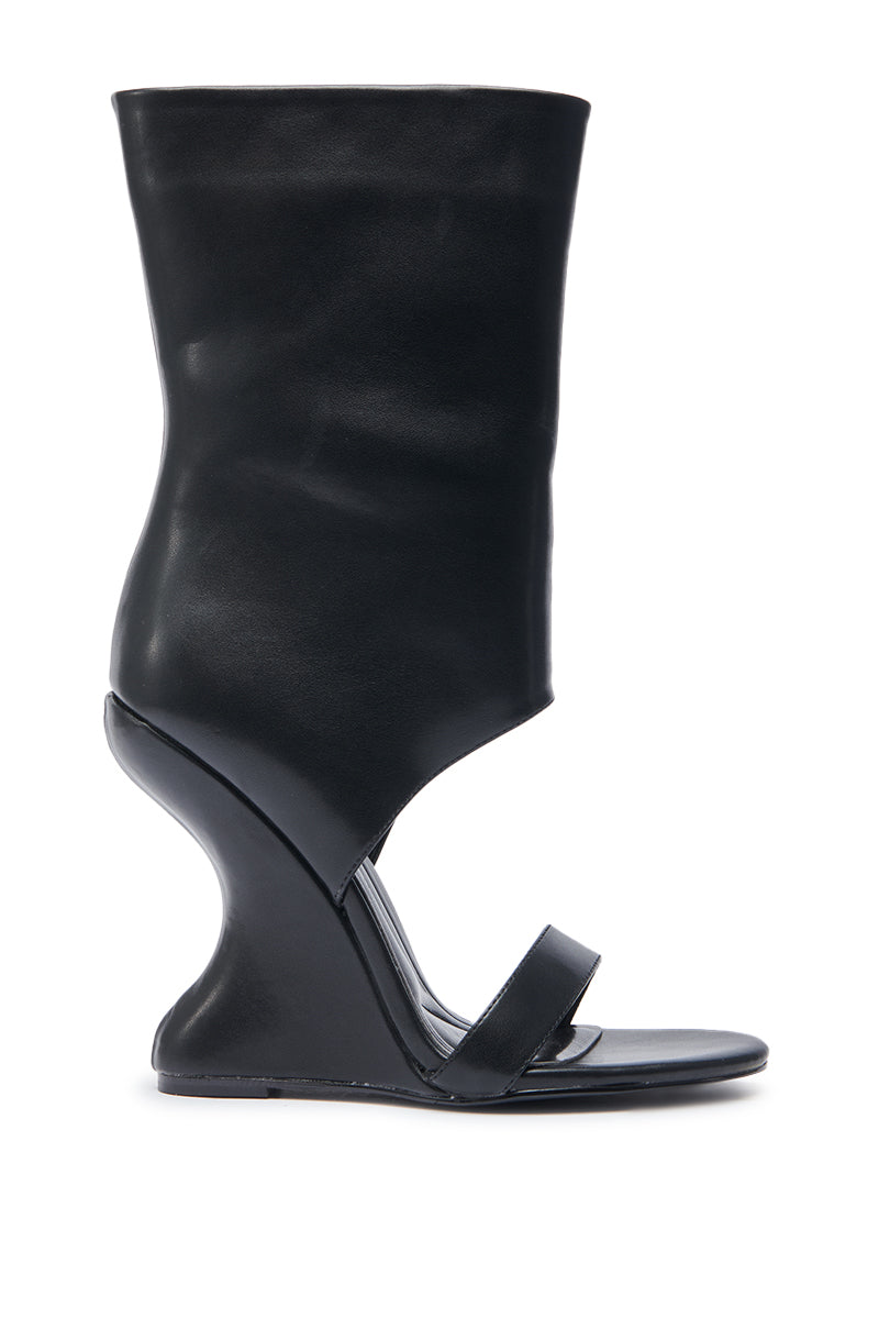 The AZALEA WANG KYVEKI BLACK WEDGE OPEN TOE BOOTIE features black faux leather, a sculptural inverted wedge heel, single toe strap, and a tall slouchy shaft above the ankle for a strikingly modern, avant-garde look.