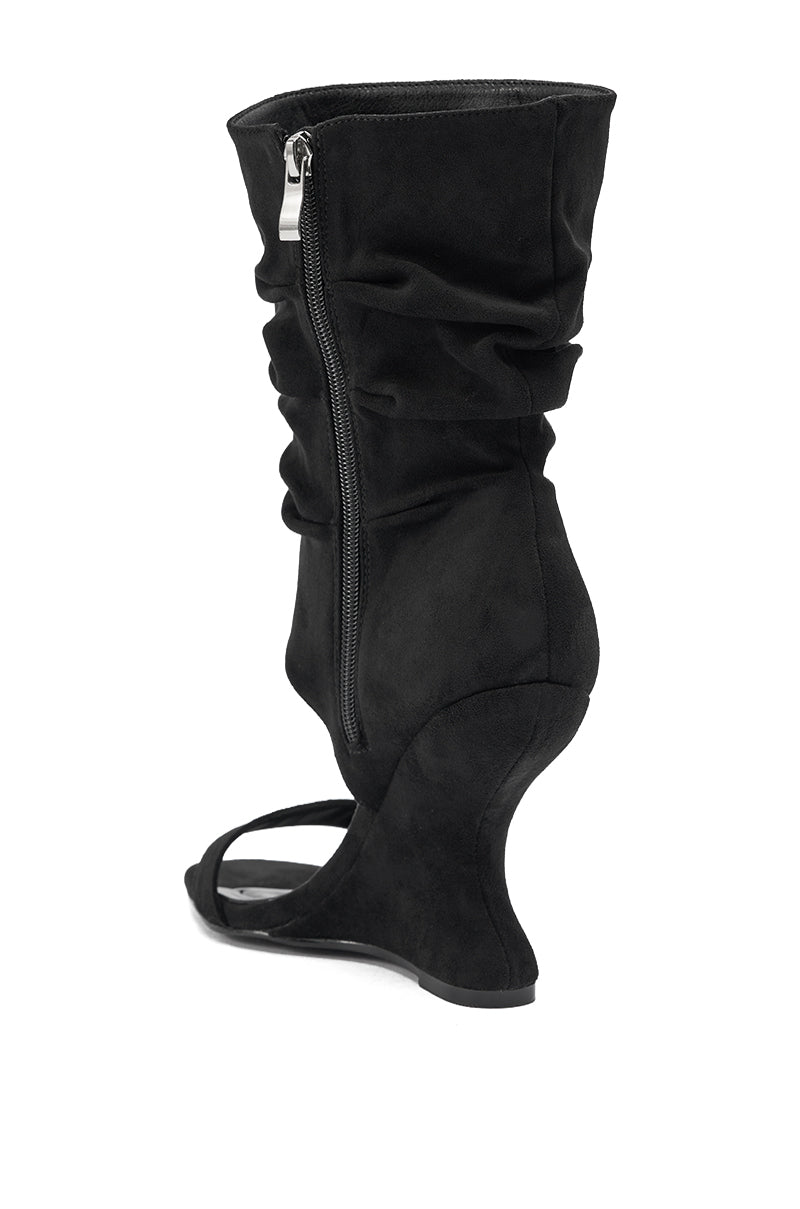 The AZALEA WANG KYVELISA Black Wedge Open Toe Bootie is a faux suede slouch boot sandal with a sculpted curved wedge heel, open toe, and side zipper, displayed from a rear side angle on a white background. 4