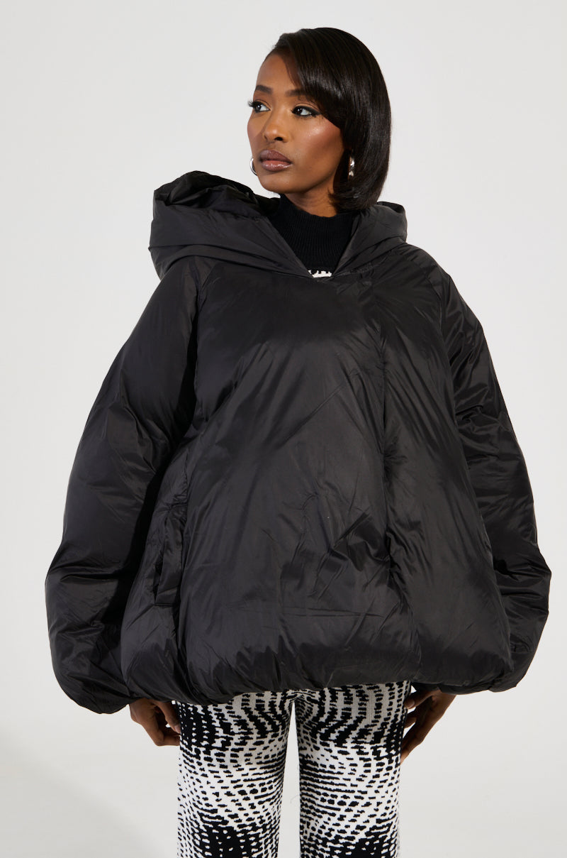 Wearing the LEONE Statement Circle Crop Puffer in black, along with black-and-white patterned pants, a person looks off to the side against a plain background.