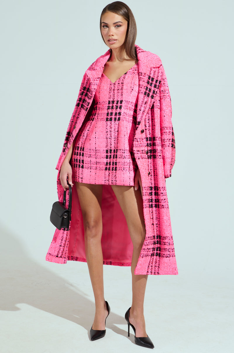 Wearing a vibrant pink plaid coat over the ELLE TWEED MINI DRESS, they hold a black handbag and wear black pointed heels, exuding Legally Blonde's confident style against a plain background.