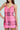 A woman channels Legally Blonde charm in an ELLE TWEED MINI DRESS, posing with one hand on her hip. The pink, black, and white plaid sleeveless dress's fitted silhouette with thin straps exudes confidence against the light background.