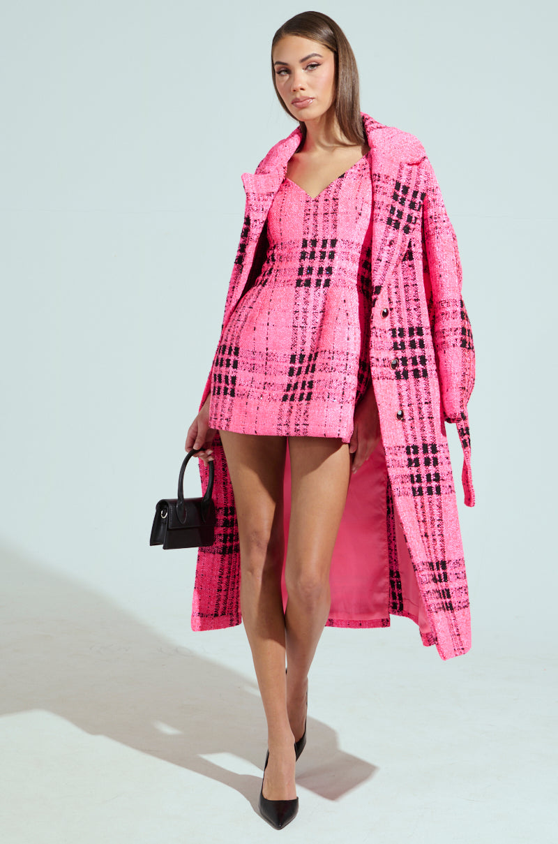 A person channels "Legally Blonde" vibes in a vibrant pink plaid ensemble, flaunting an ELLE TWEED MINI DRESS and matching long coat. They sport a small black handbag and black pointed heels, confidently standing against a plain light background.