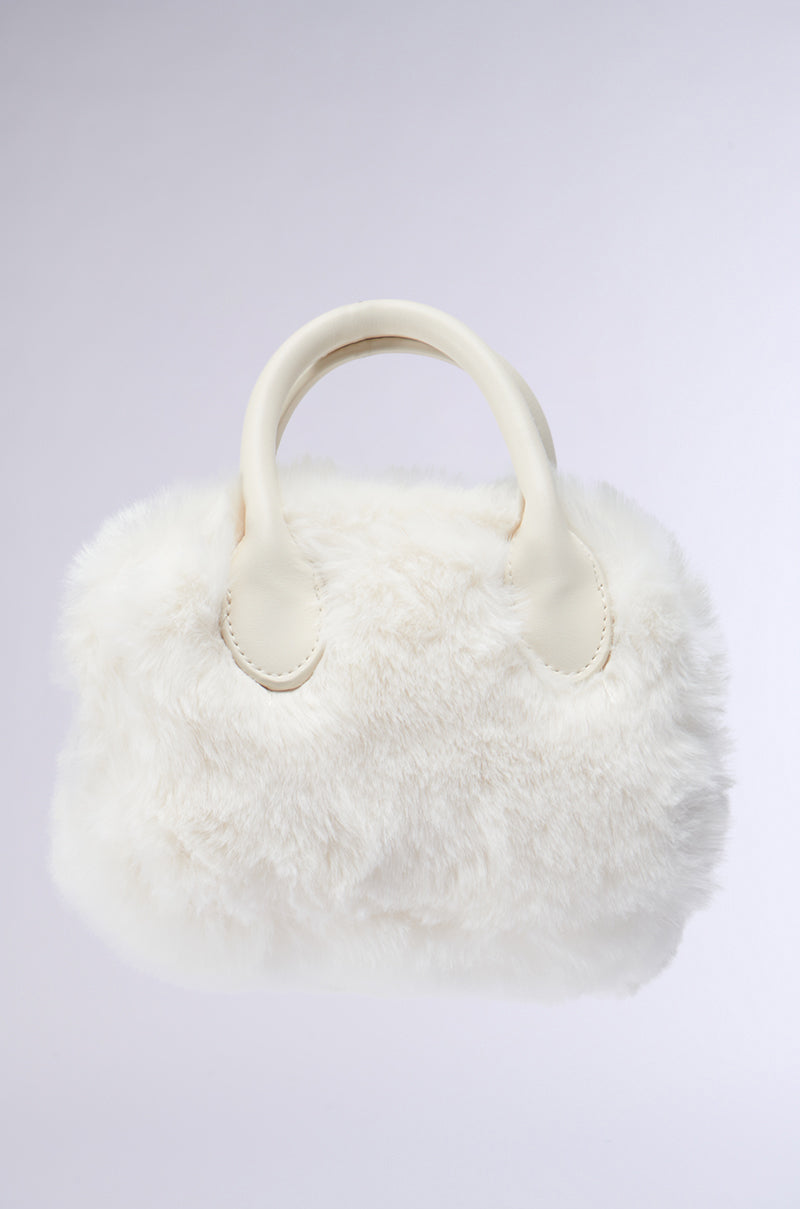 The APRES SHERPA BAG by Rag Company LLC is showcased against a simple background. This small, plush handbag features a fluffy white exterior and two sturdy handles. Its faux fur design emanates a soft, cozy vibe, making it perfect for stylish, casual outings.