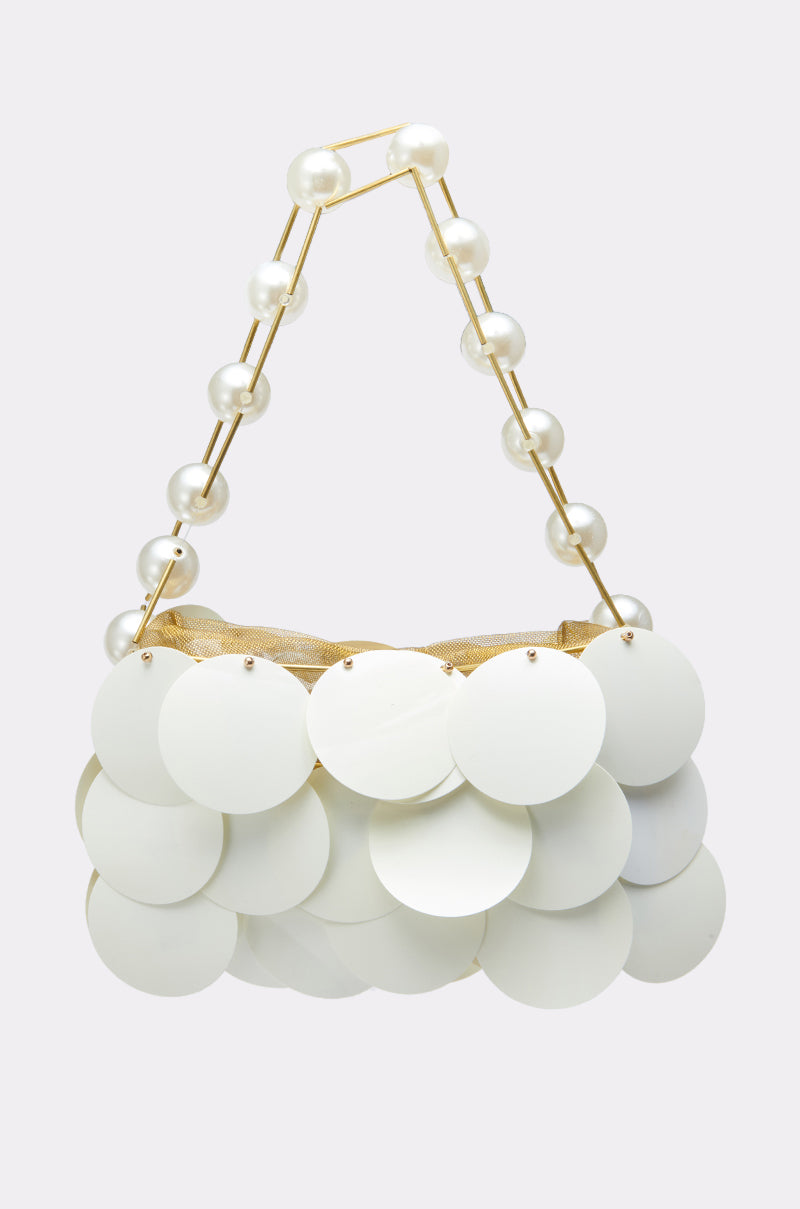 The GIVING CLASSY SEQUIN PURSE is a chic mini handbag with large white circular discs, a gold handle decorated with oversized pearl hardware, displayed on a light gray background.