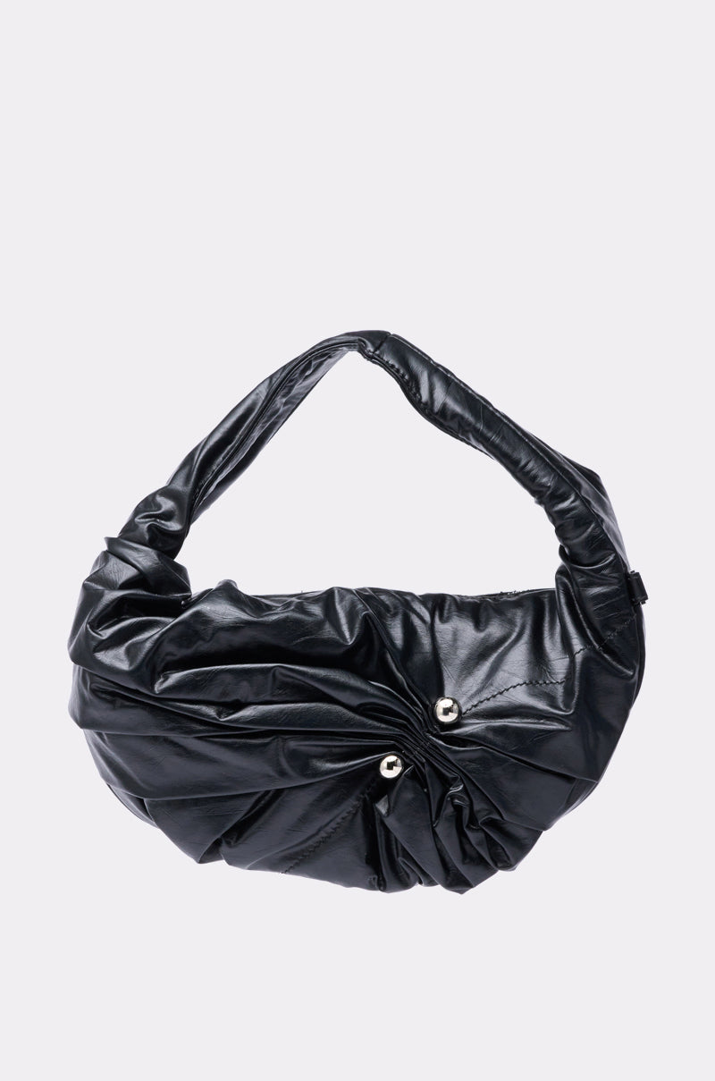 The NEW PIERCING PURSE by AKIRA Label is a black ruched faux leather bag with a twisted handle and two silver studs on the front, shown against a light gray background. 1
