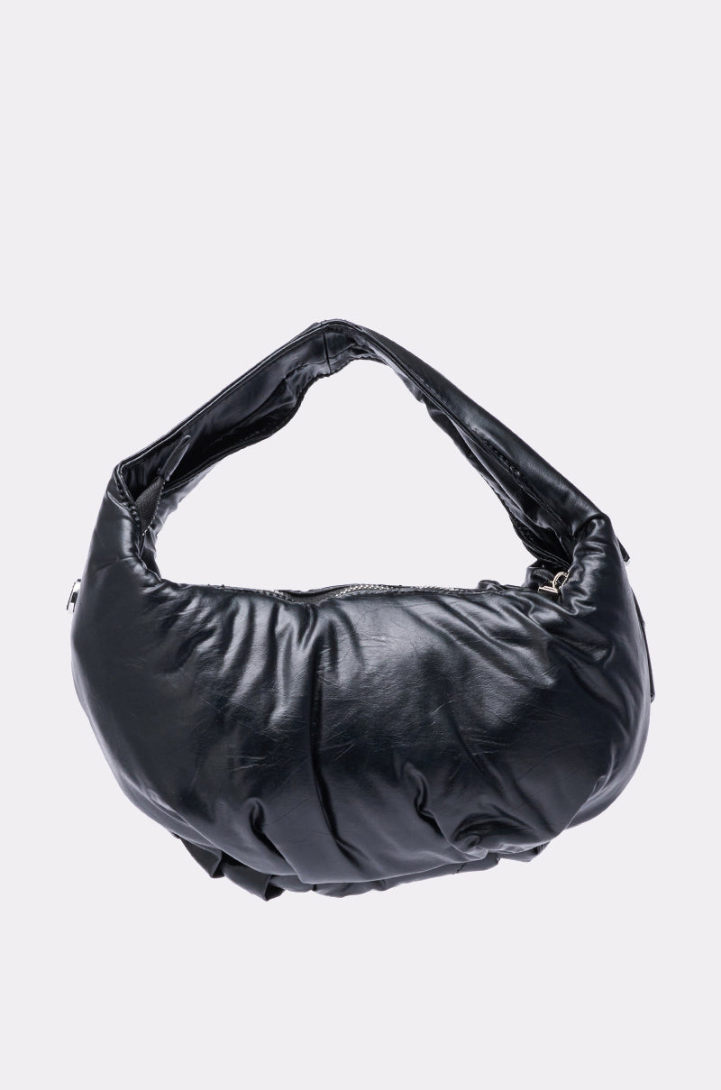 The NEW PIERCING PURSE is a shiny black, puffy faux leather crescent-shaped bag with a short handle and silver-tone hardware, shown against a plain light gray background.