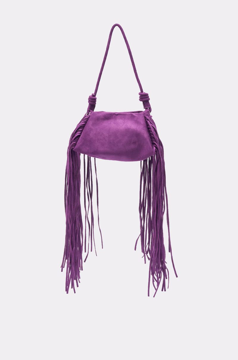 The IN THE WIND SUEDE PURSE is a small purple bag with fringe on both sides and a single handle, displayed against a plain light background.