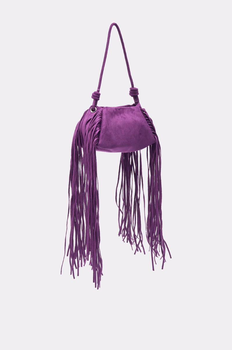 The IN THE WIND SUEDE PURSE is a purple baguette-style bag featuring a single handle and long, thin fringe on both sides, displayed against a plain light background.