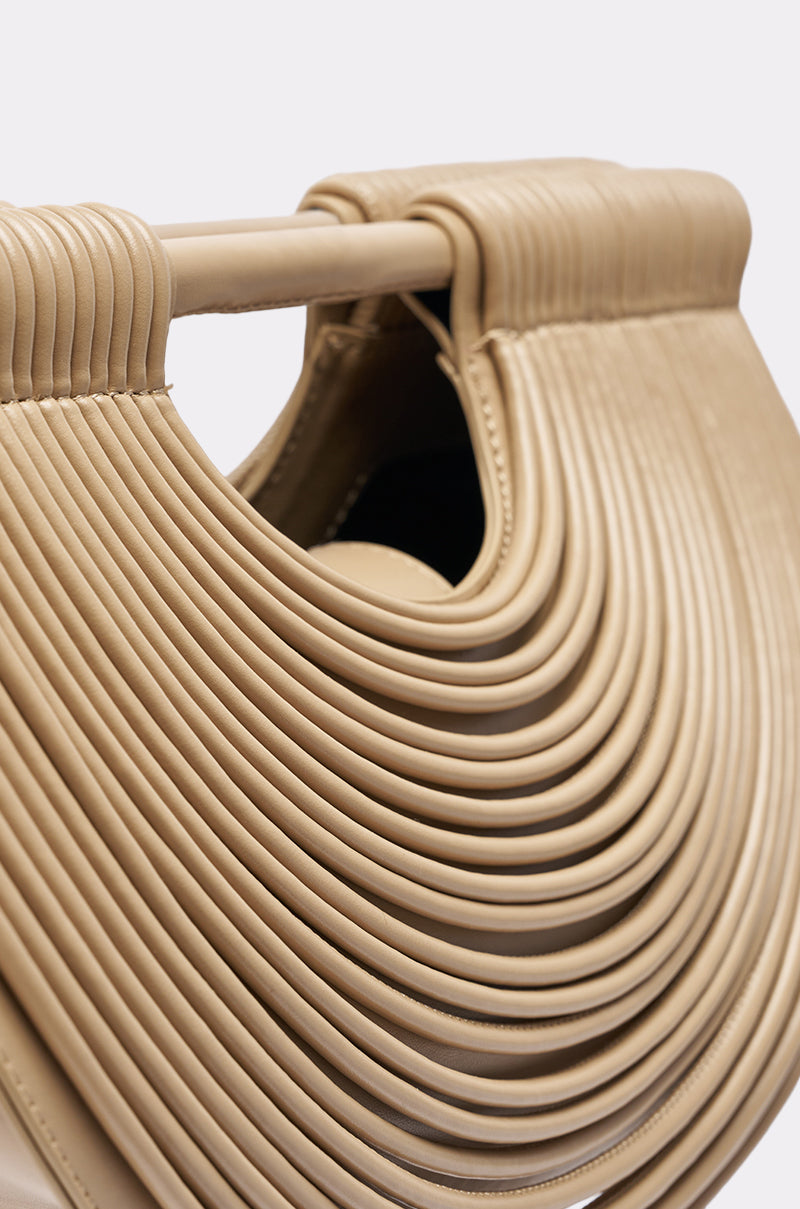 Close-up of the CRESCENT CARRY-ALL PURSE in beige, featuring curved, layered ridges, a sturdy handle, detailed texture, and a half-moon silhouette that highlights its modern faux leather design.