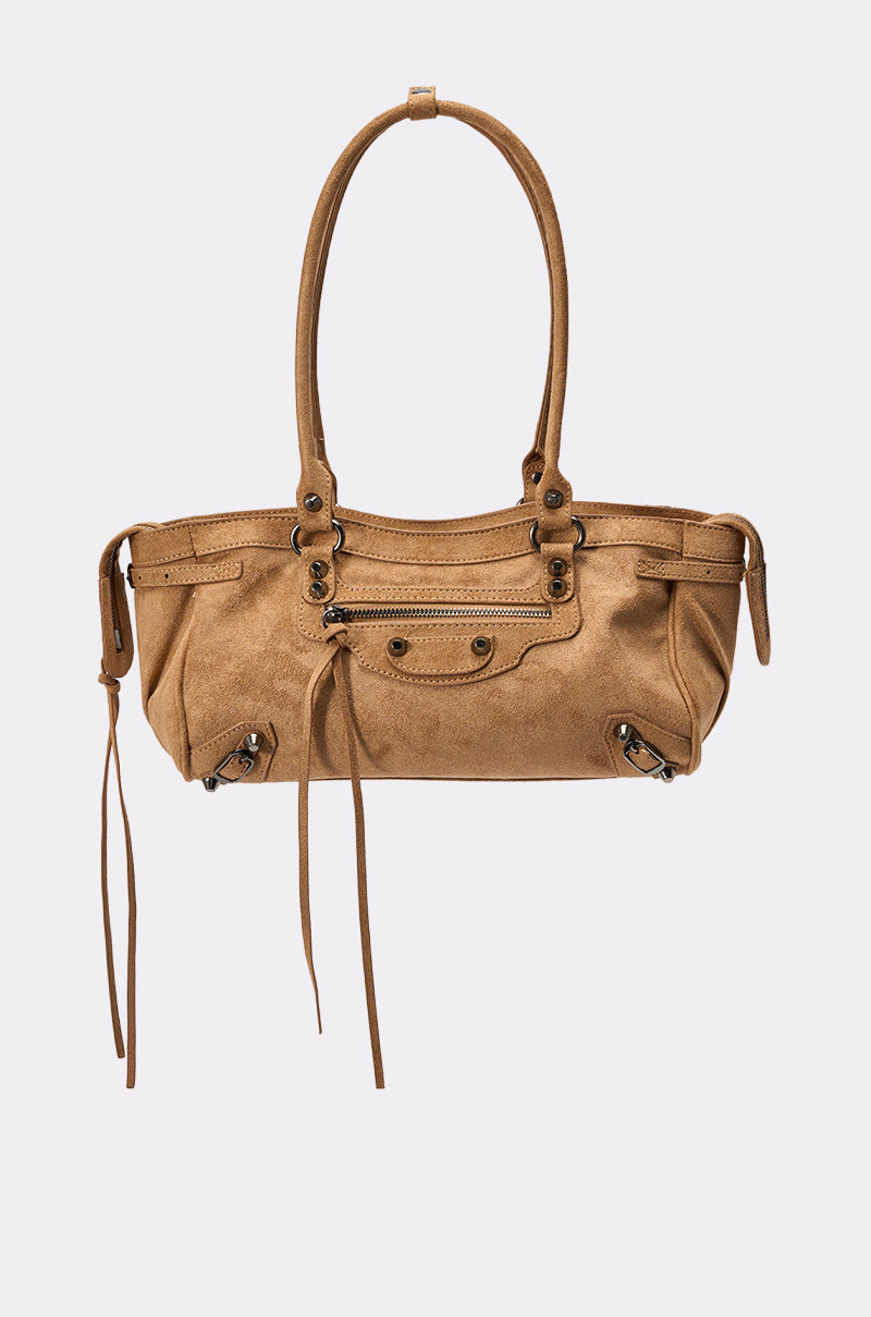 The IN THE CITY BAG is a tan leather handbag with double handles, a front zipper pocket, decorative buckles, and long leather tassels, capturing the charm of a brown suede shoulder bag on a plain light background. 0