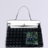 Introducing the TYPE IT OUT KEYBOARD PURSE: a handbag made from recycled computer keyboard parts, featuring black keys and an exposed circuit board. Its design combines classic style with faux patent leather, merging tech with fashion on a plain white backdrop.