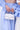 Two people in light blue and white stripes are shown from the torso down. One holds the HONEYMOON LACE APPLIQUE BAG, a chic satin handbag with a textured white design and top handle. No faces are visible; focus is on the bag.