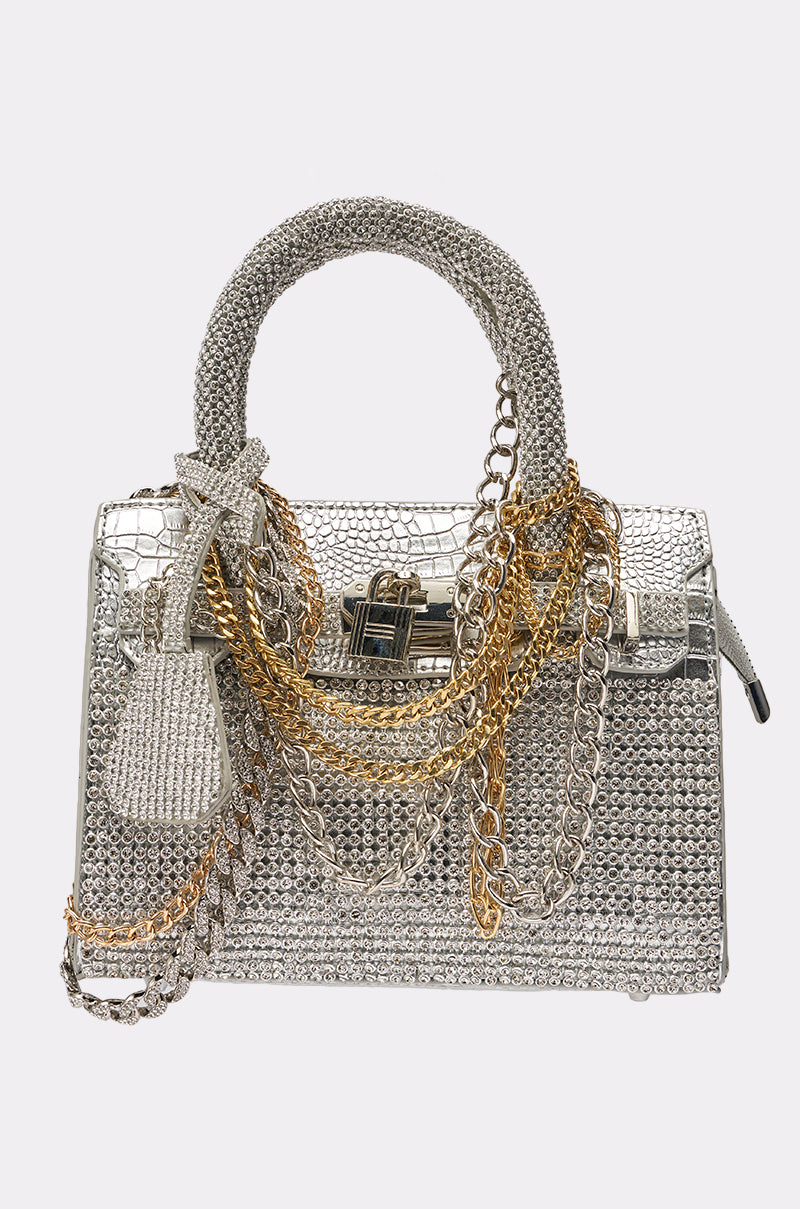 The TOP NOTCH EMBELLISHED CHAIN PURSE is a sparkling rhinestone handbag in metallic silver with silver and gold chains, a textured handle, and a decorative key charm.