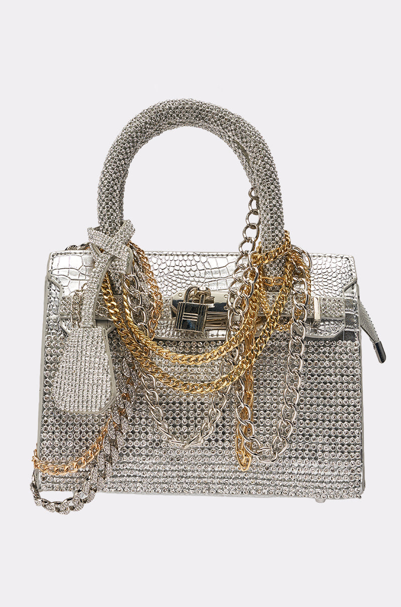 The TOP NOTCH EMBELLISHED CHAIN PURSE is a sparkling rhinestone handbag in metallic silver with silver and gold chains, a textured handle, and a decorative key charm. 0