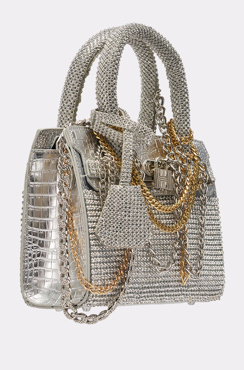 The TOP NOTCH EMBELLISHED CHAIN PURSE is a sparkling silver bag with rhinestones, gold and silver chains, a crocodile-like texture, and a matching accessory attached to the handle.