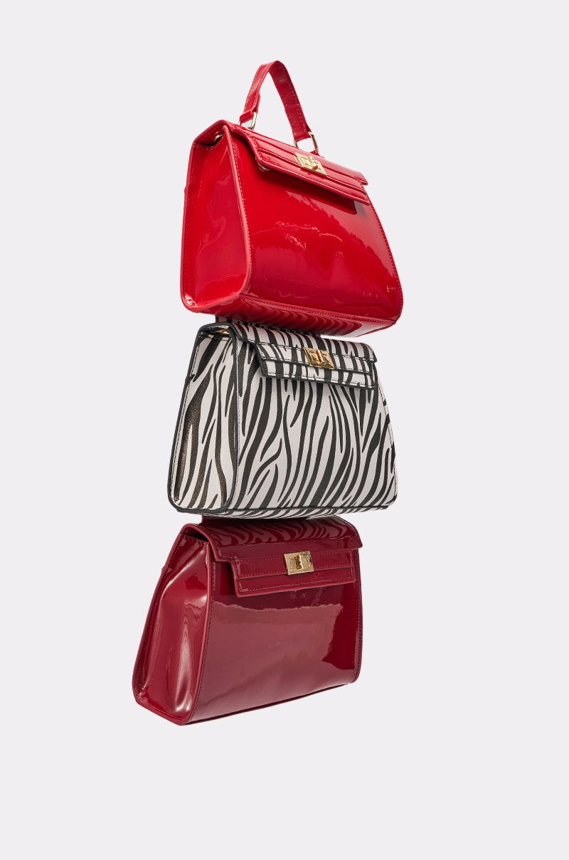 The WILD ONE STACKED DETACHABLE PURSE TRIO features two shiny red faux leather purses and a zebra print bag, all with gold clasps, stacked vertically against a plain light background. 2