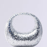The ALWAYS ADD SPARKLE HARD SHELL PURSE is a glittering silver handbag with metallic sequin detailing, a rounded shape, and a wide circular handle, set against a light gray backdrop.