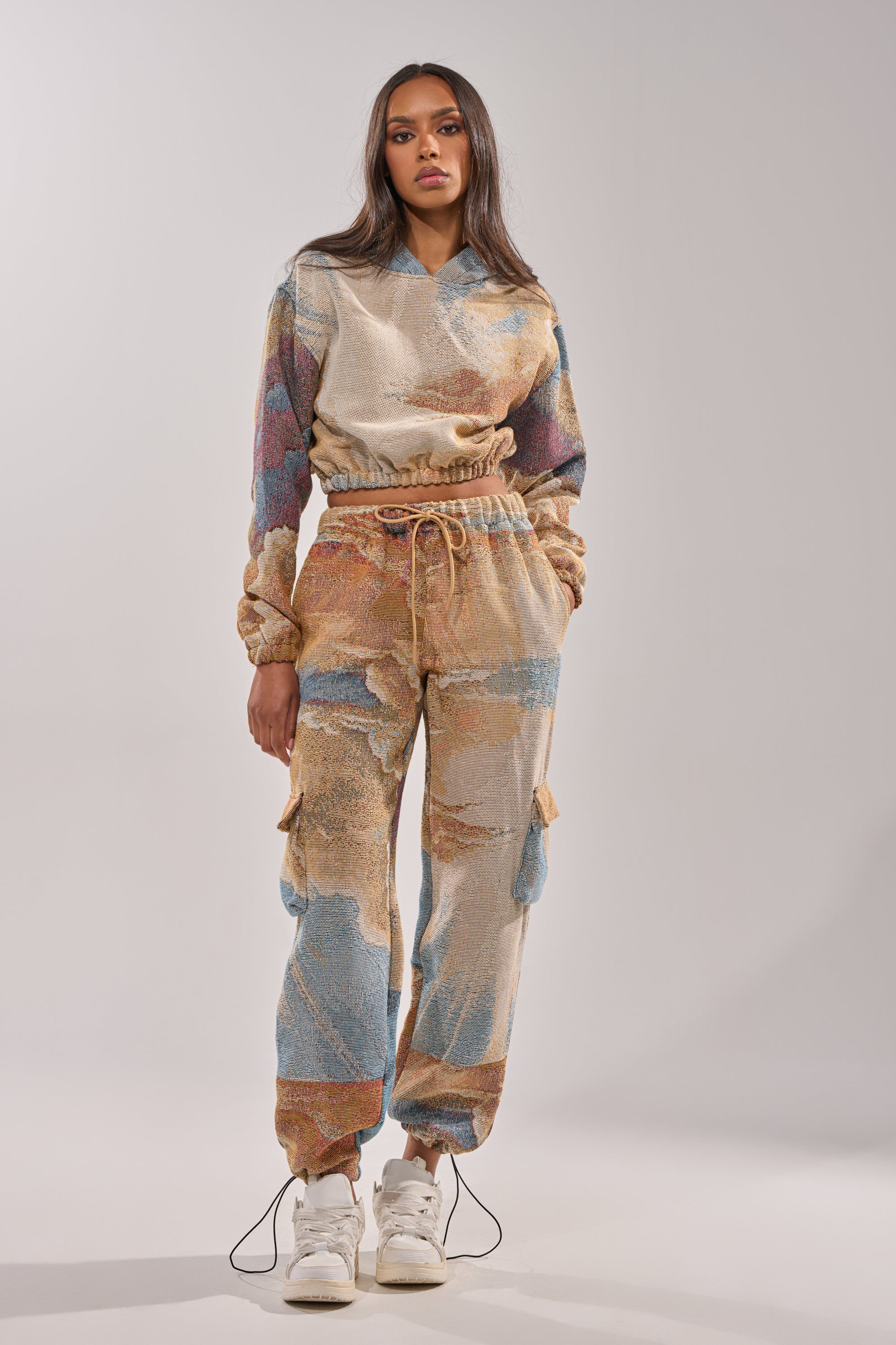 A woman stands facing forward in the INTO THE WILD WIDE LEG JOGGER set, featuring colorful abstract patterns and drawstrings, paired with white sneakers against a plain light background. 5