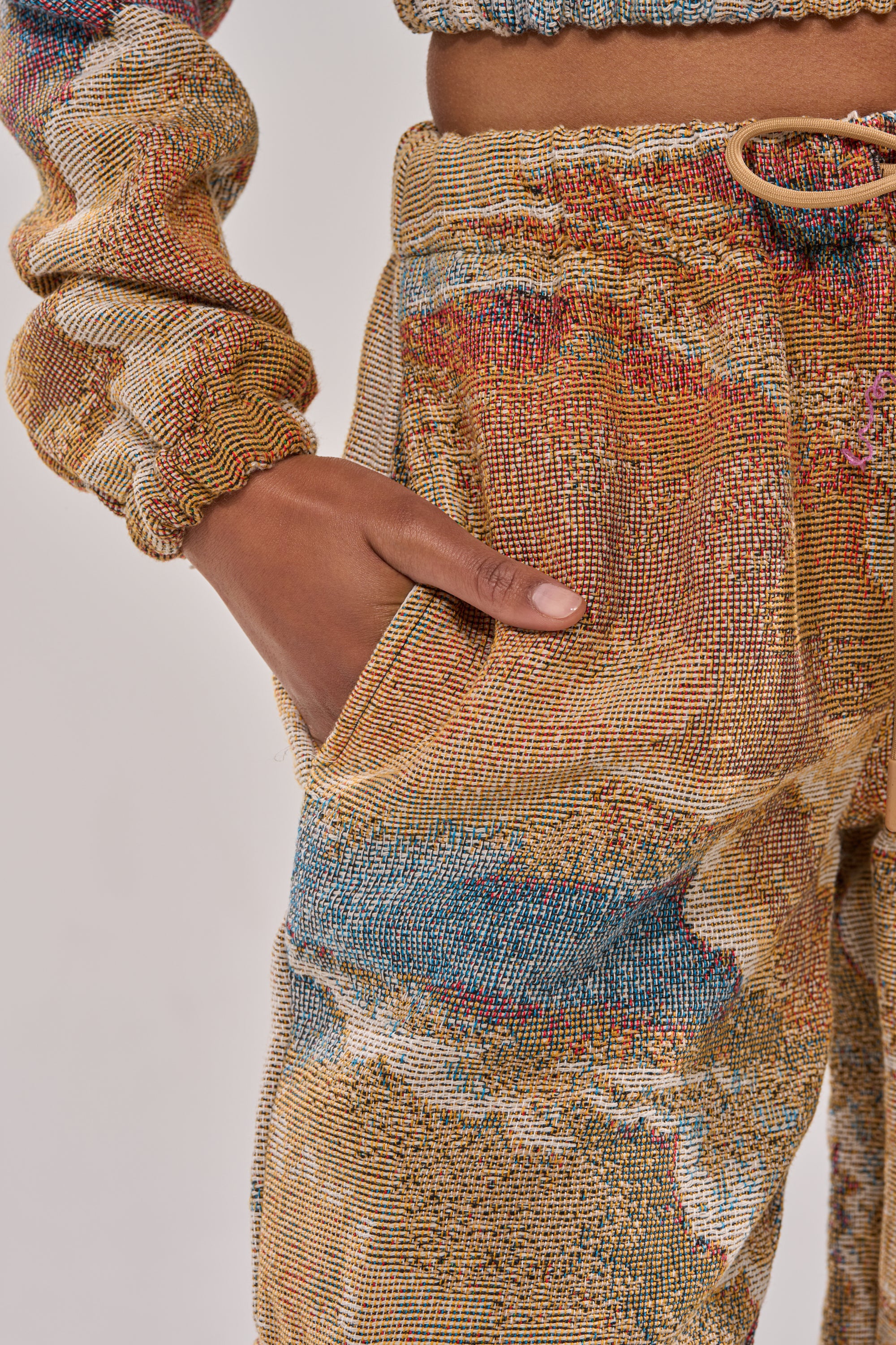 A close-up of a person wearing the INTO THE WILD WIDE LEG JOGGER with their hand in the pocket, showcasing an abstract woven pattern in earthy tones, blues, and reds. 6