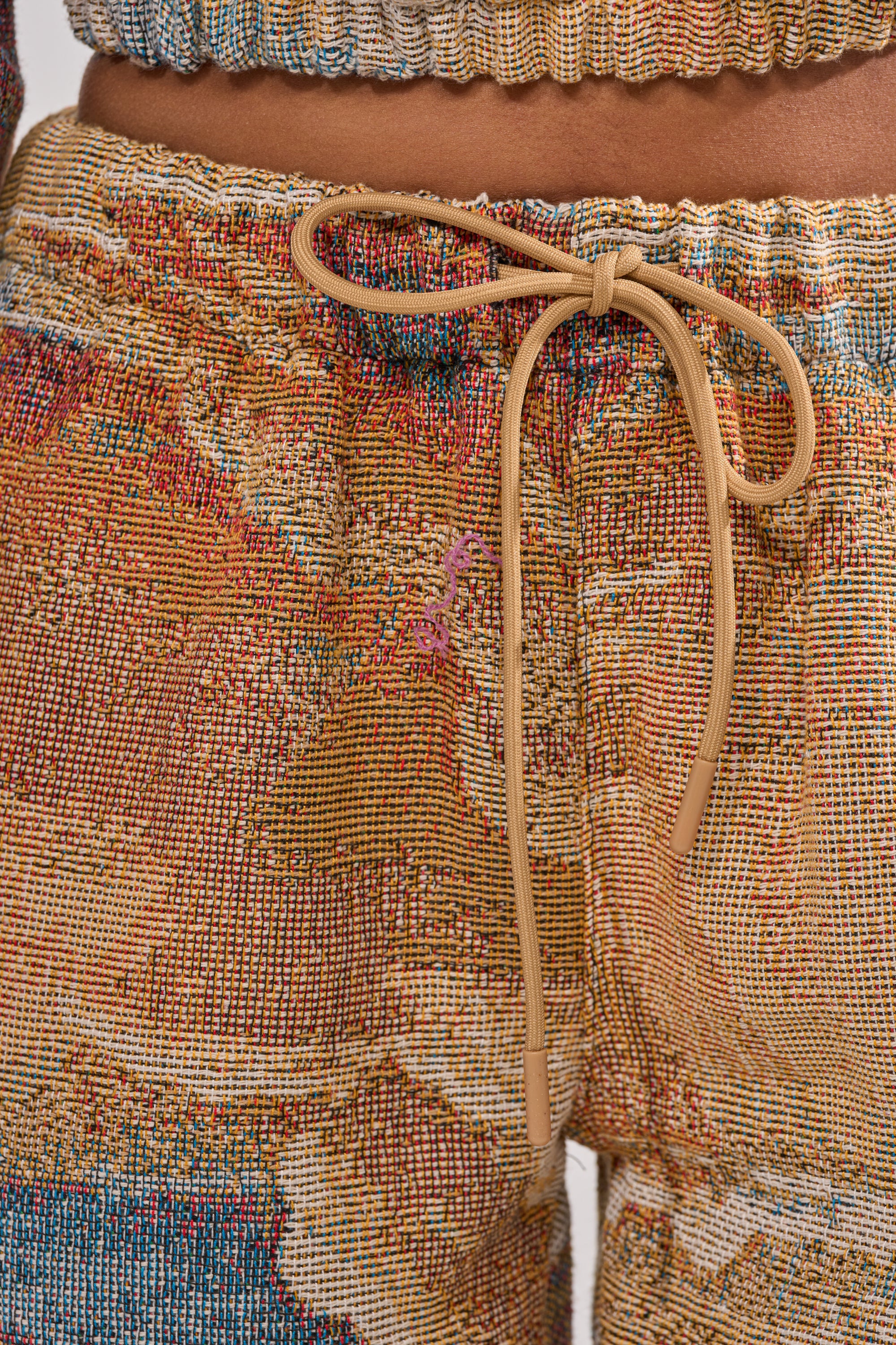 Close-up of a person wearing INTO THE WILD WIDE LEG JOGGER pants featuring an elastic waistband, tan drawstring, and abstract landscape-inspired patterns in vibrant, multicolored fabric. 8