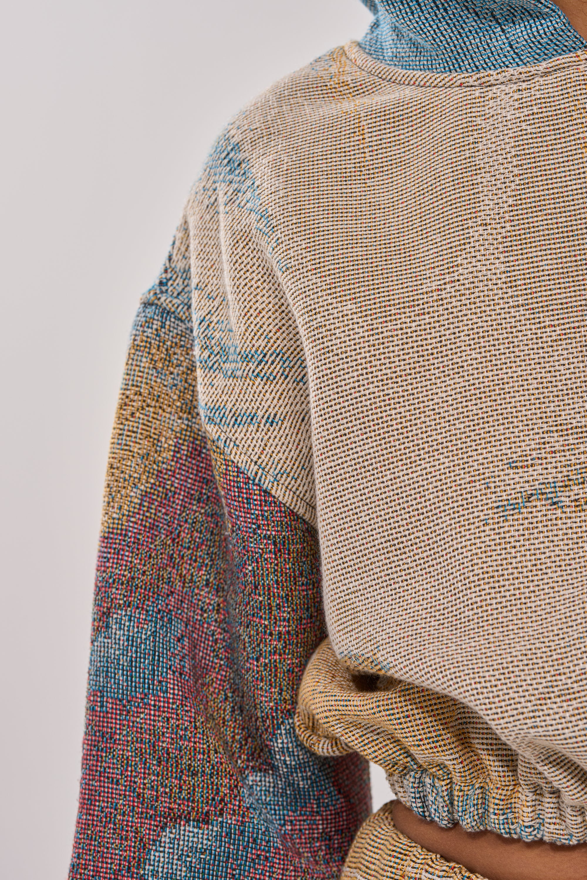 Close-up of the INTO THE WILD SWEATSHIRT, a multicolored woven piece in beige, blue, yellow, and red with a scenic landscape pattern and elastic cinched waist, evoking vintage streetwear style. 7