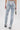A person wearing the LACE IT UP SKINNY DENIM PANT, featuring a light-wash, high-rise fit with lace-up detail on the back and ruched legs, holds a silver chain purse and is photographed from behind against a plain background.