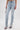 A person wears the LACE IT UP SKINNY DENIM PANT—light-wash, high-waisted jeans with corset lace-up details—styled with open-toe chain sandals and a metallic chain purse against a plain white background.