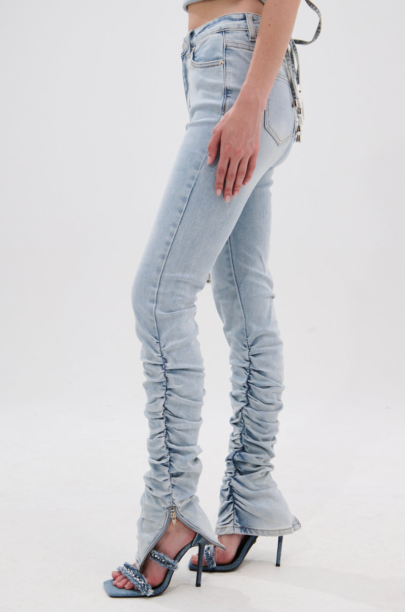 A model wearing the LACE IT UP SKINNY DENIM PANT with ruched skinny fit and zippered hems, paired with high-heeled sandals, is shown from the waist down against a plain white background. 3