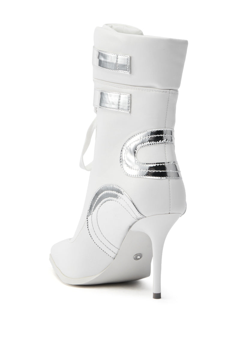 The AZALEA WANG LACIE SILVER SPORTY BOOTIE is a stylish white vegan leather bootie with metallic detailing, decorative side stitching, a pointed toe, stiletto heel, and two horizontal silver straps near the top.