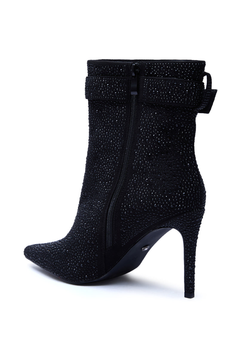 The AZALEA WANG LAKSHMI BLACK SPARKLE RHINESTONE STILETTO BOOTIE is a black suede ankle boot with a pointed toe, side zipper, sparkling rhinestones, plus a decorative strap and bow at the upper ankle for added elegance.