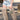 A person stands on a sunny street with industrial structures in the background, wearing a beige peplum top, ripped denim shorts, and AZALEA WANG LAGANN BONE THIGH HIGH FUR LUXE BOOTS, holding a small metallic purse.