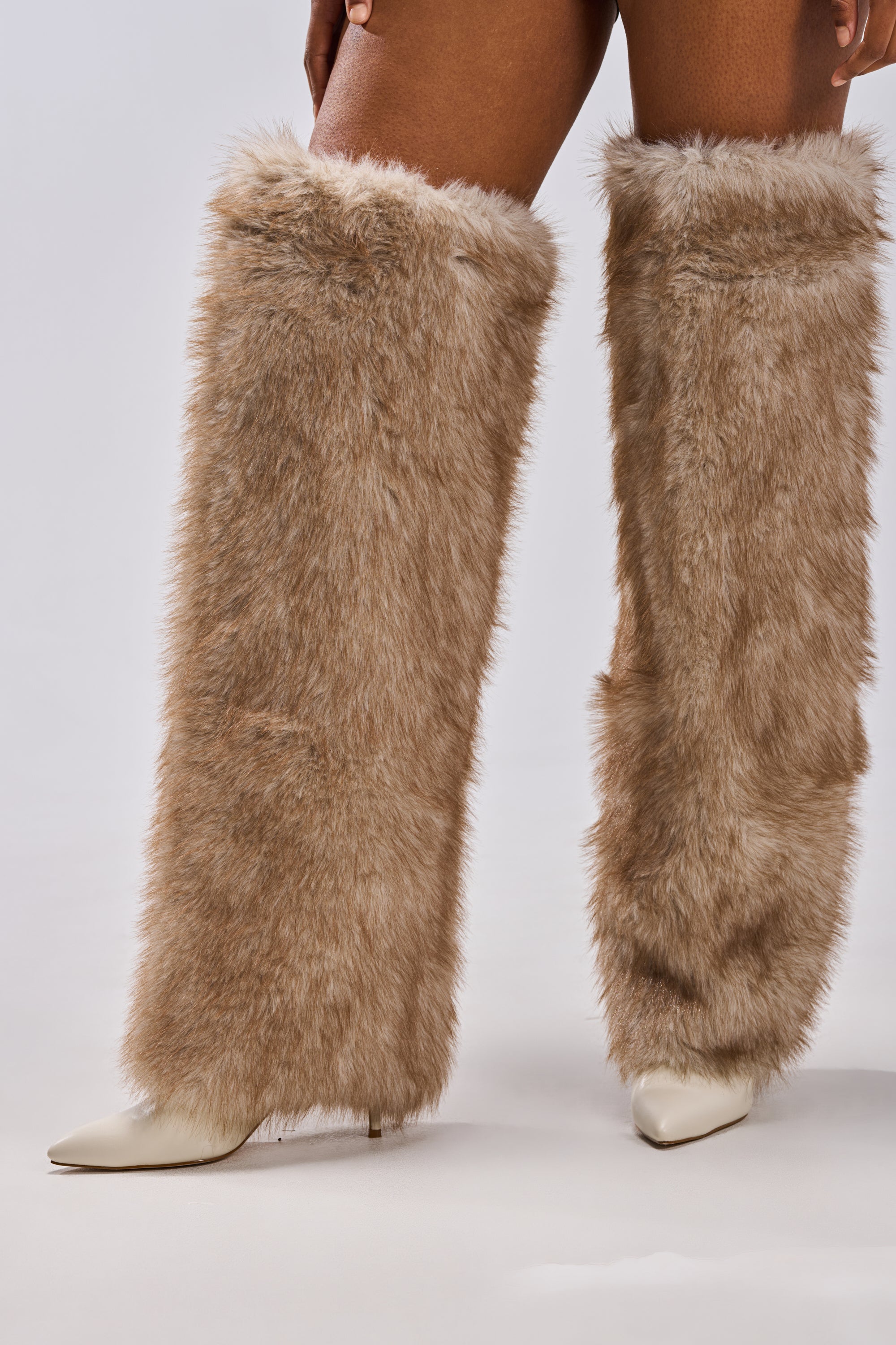 Someone stands against a light gray background wearing AZALEA WANG LAGANN BONE THIGH HIGH FUR LUXE BOOTS—tall, fluffy, light brown thigh-high boots with stiletto heels.